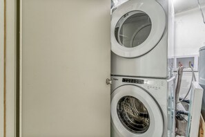 A stacked washer and dryer unit with a control panel and hoses visible. - Cozy Kensington Suite | Sleeps 6 | 1BR + Sofa Bed (Calgary)