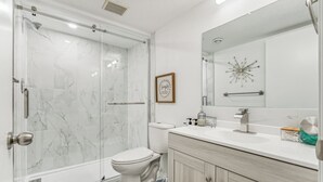 Un bagno moderno con doccia a vetro, un water, un lavabo con specchio e una citazione incorniciata al muro.