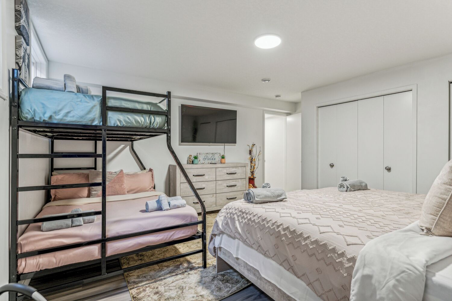 Ein Schlafzimmer mit Etagenbett, Flachbildfernseher, Kommode und Kleiderschrank.