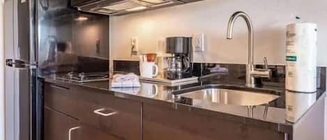 Una cocina moderna con un refrigerador de acero inoxidable, una cafetera y un lavamanos.