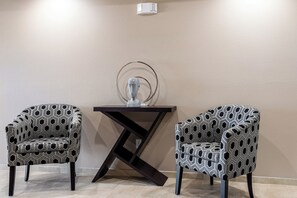 Duas poltronas estampadas, uma mesa de madeira escura com uma escultura de vidro e uma parede lisa.