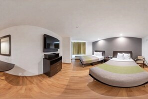 Ein modernes Hotelzimmer mit einem gewölbten Holzboden, einem Flachbildfernseher, einem Bett mit einer grün-weiß gestreiften Tagesdecke und einem Nachttisch mit einer Lampe.