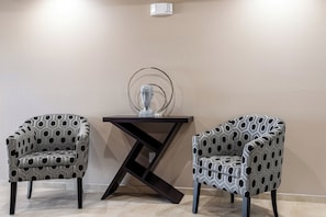 Duas poltronas estampadas, uma mesa de madeira escura com uma escultura de vidro e uma parede lisa.
