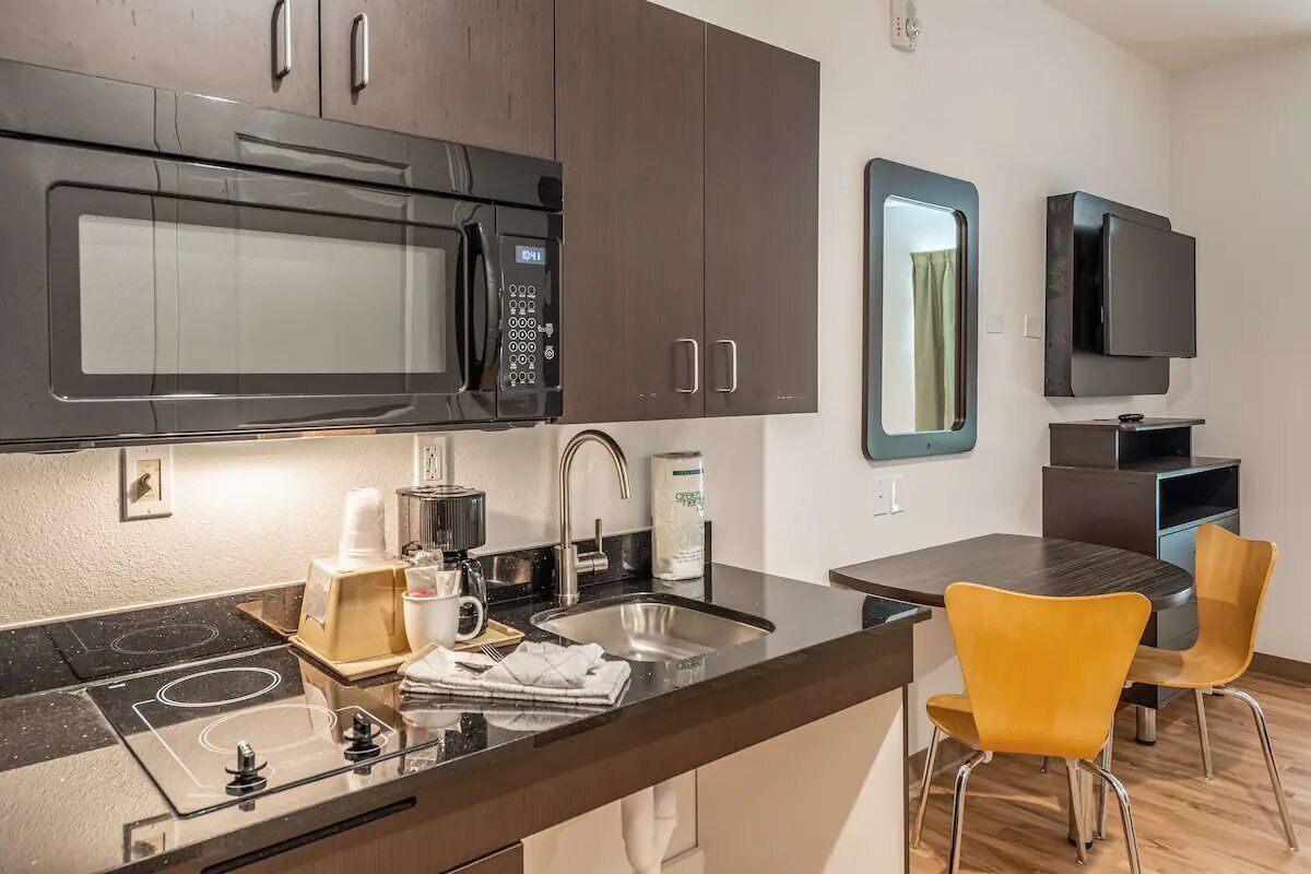 Una cocina moderna con microondas, estufa, pileta y sillas amarillas.