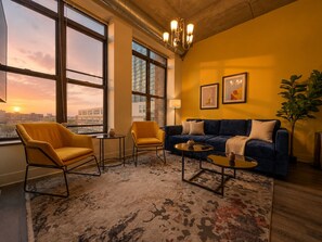 Un salon moderne comprenant un canapé, deux fauteuils, une table basse et une grande fenêtre donnant sur la ville.