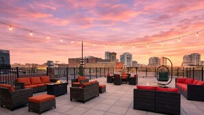 En tagterrasse med udendørs møbler, lyskæder og udsigt til byens skyline.