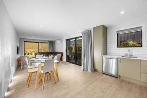 A modern kitchen with a dishwasher, a dining area with a table and chairs, and a sliding glass door leading to a balcony. - 3-bed in Northlake | Bikes, Boards & Wānaka Bliss (Wānaka)