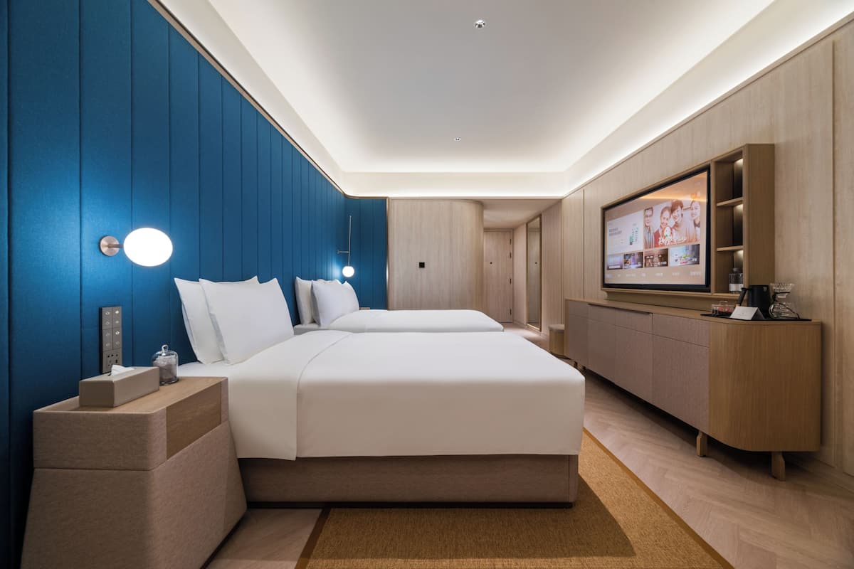 A modern hotel room with a large bed, a TV, a desk, and a built-in wardrobe.