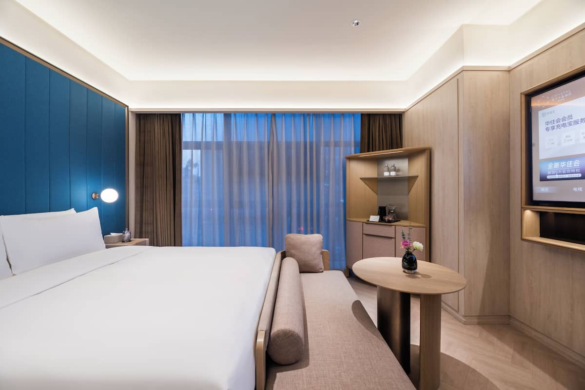 Habitación de hotel con una cama grande, un escritorio con silla, televisor y ventana con cortinas.