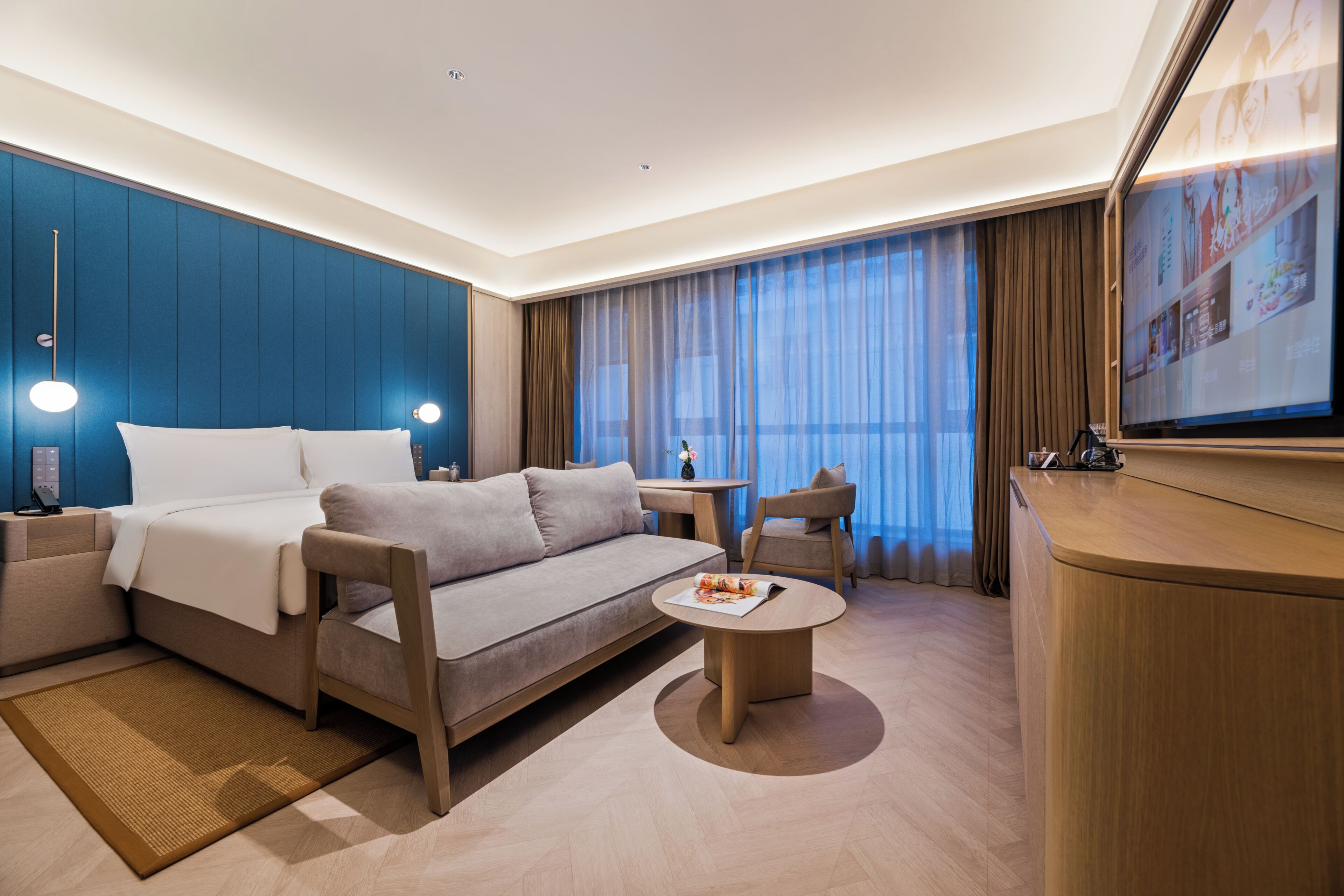 Ein modernes Hotelzimmer mit Bett, Sofa, Couchtisch und einem Fernseher.