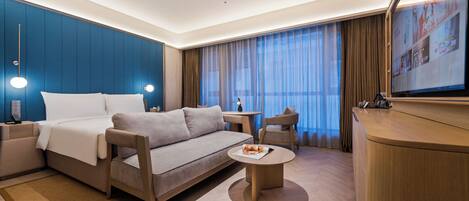 Ein modernes Hotelzimmer mit Bett, Sofa, Couchtisch und einem Fernseher.
