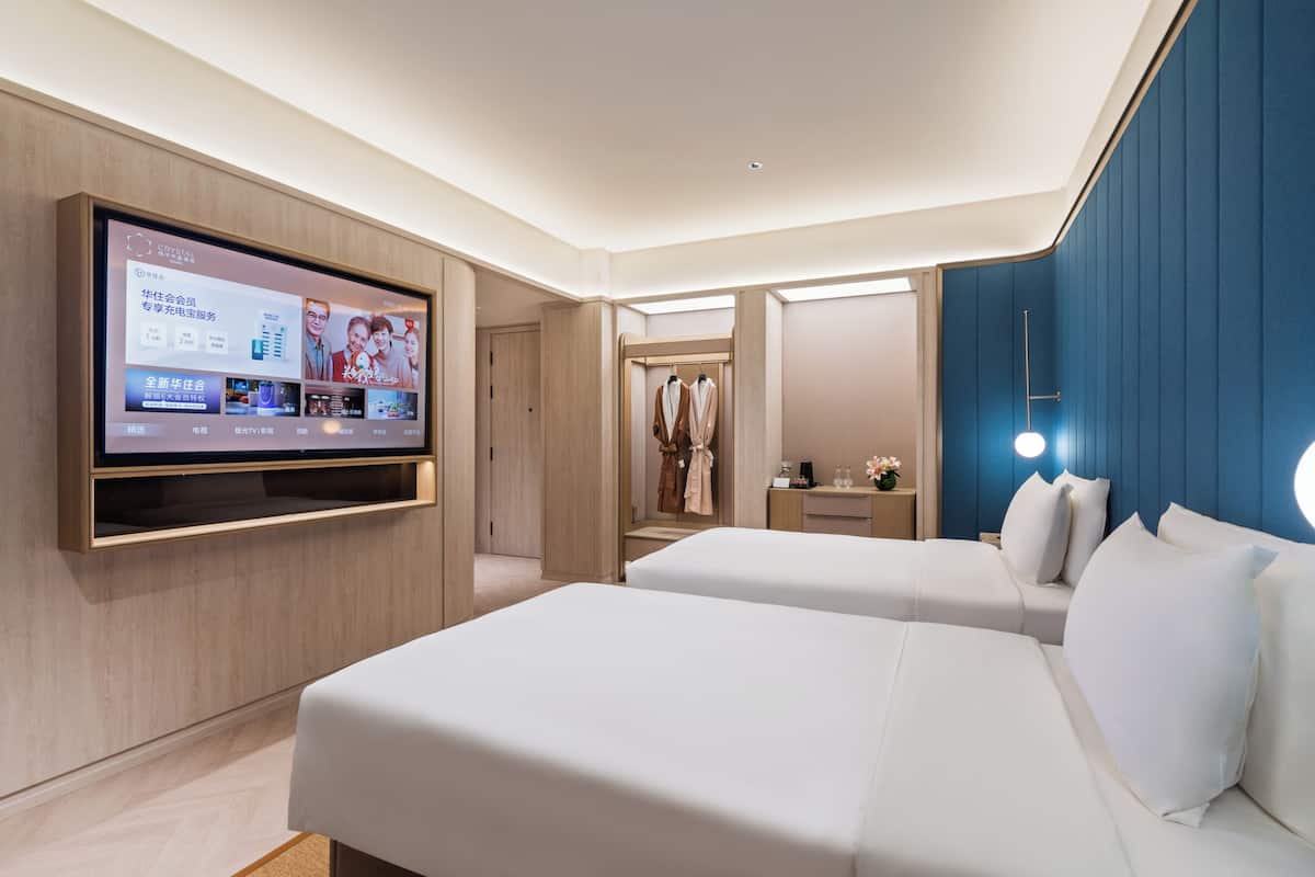 Habitación de hotel con televisión montada en la pared, dos camas, un escritorio y un armario.