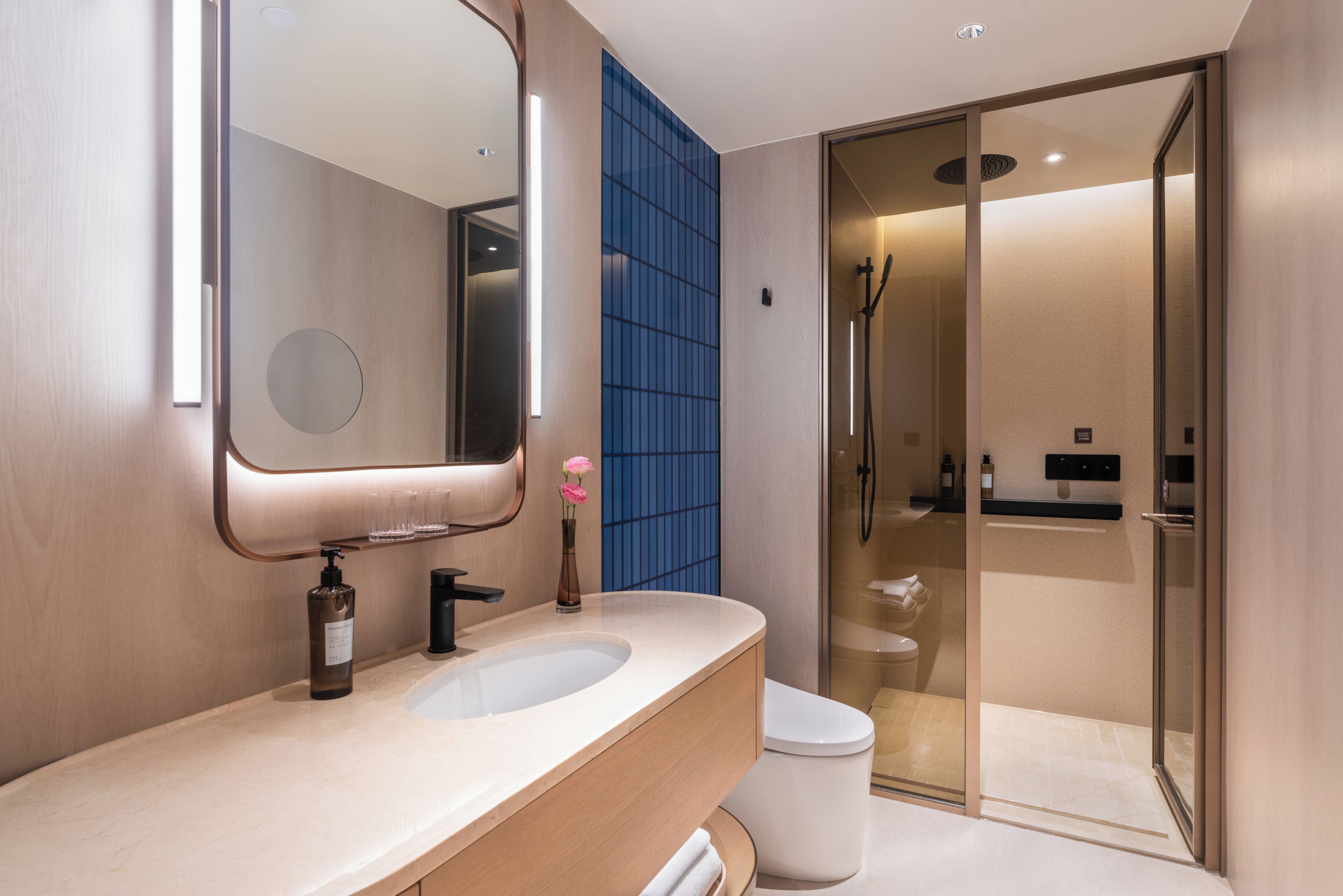 A modern bathroom with a large mirror, two sinks, a toilet, and a glass-enclosed shower area.