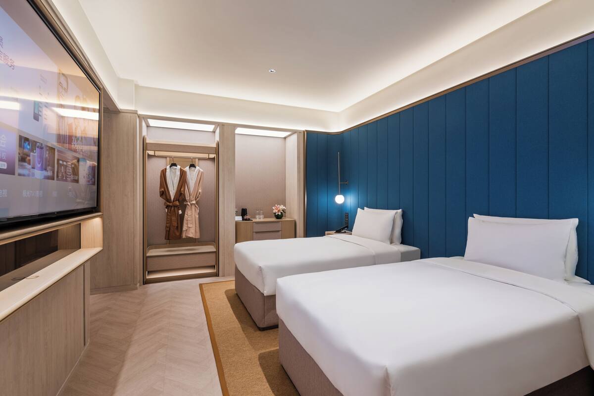 Una habitación de hotel con dos camas, televisión, armario y escritorio con lámpara.