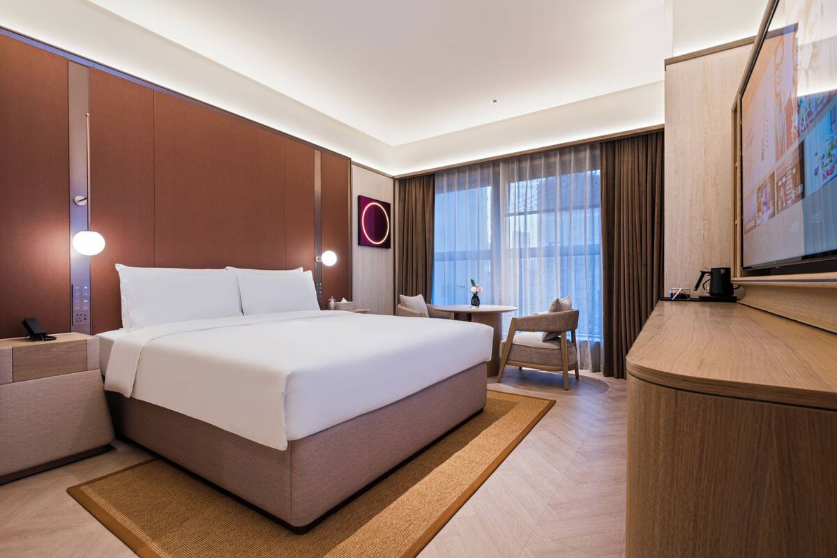 Una habitación de hotel con una cama grande, un escritorio, una silla, un televisor y una ventana con cortinas.