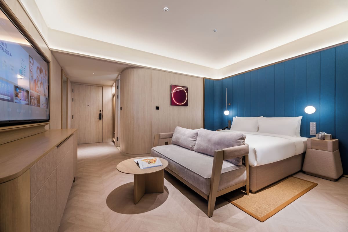 Una habitación de hotel moderna con una cama, un sofá, una mesita y un televisor.