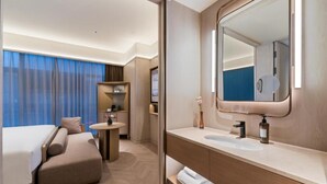 Una camera d'albergo con un letto, un tavolino rotondo, uno specchio e un piccolo bagno.