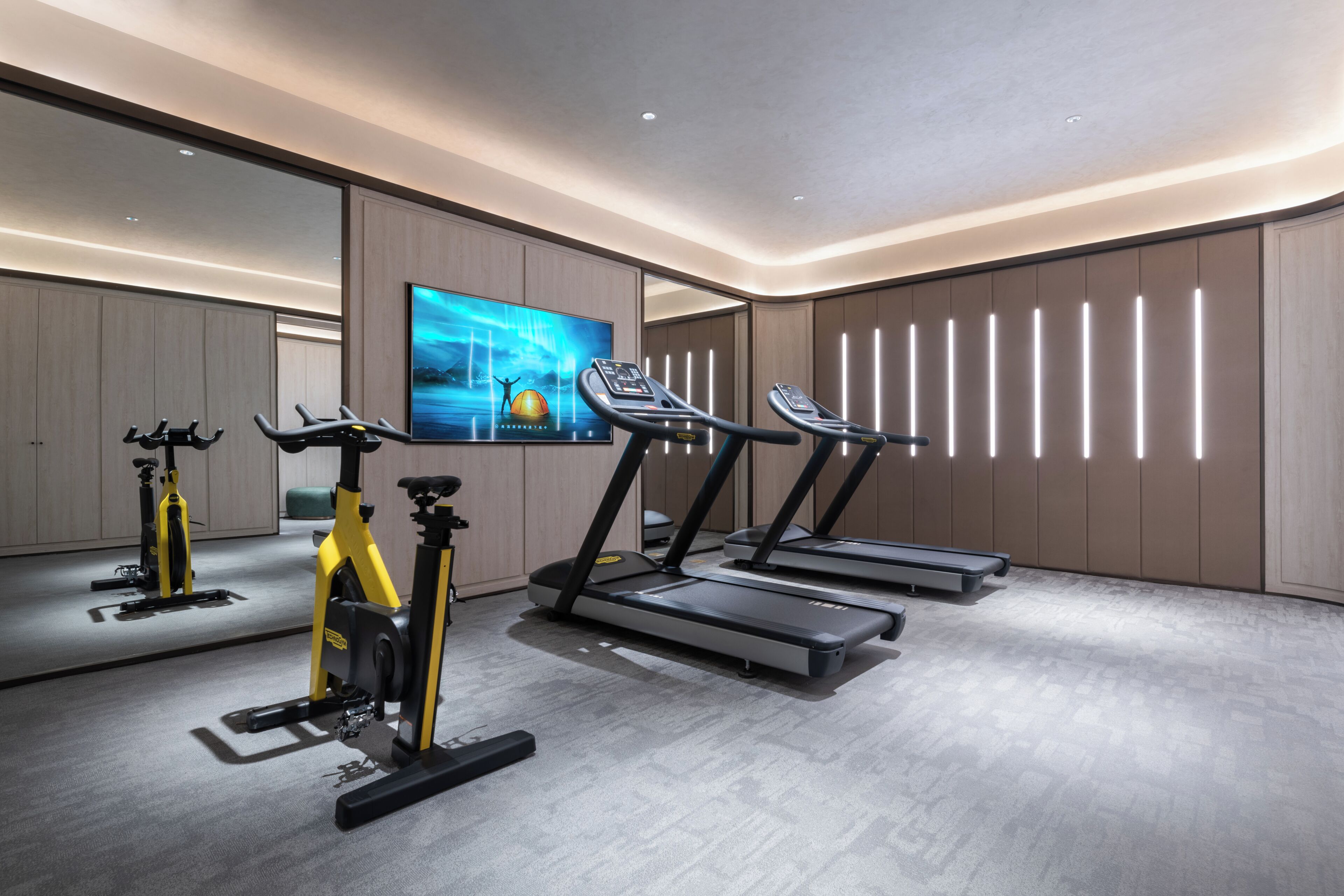 A modern gym with stationary bikes, treadmills, and a large TV screen.