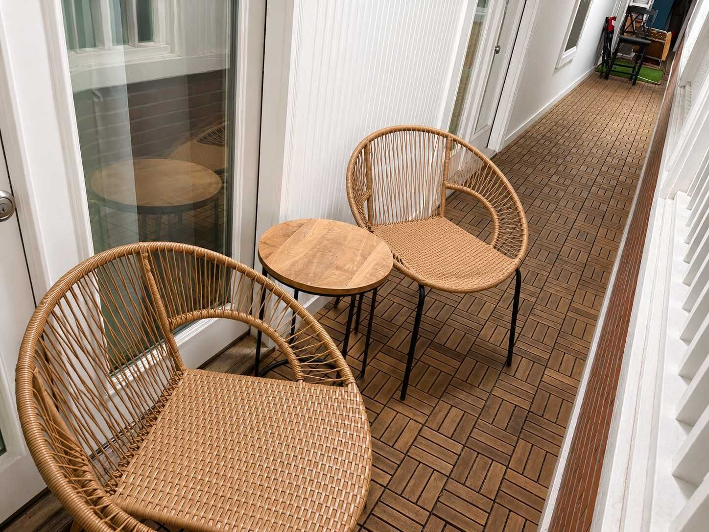 Een gang met een patroon vloer, twee rieten stoelen en een glazen deur.