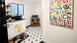 Eine Küche mit weißen Schränken, einem schwarzen Kühlschrank, einer Spüle und einer Mikrowelle. Der Boden hat ein Sternenmuster und an der Wand hängt ein farbenfrohes Kunstwerk mit der Aufschrift 'LOVE YOU'.