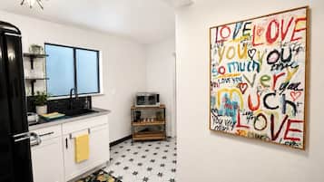 Een keuken met witte kastjes, een zwarte koelkast, een dubbele spoelbak en een magnetron. De vloer heeft een stermotief en op de muur hangt een kleurrijk kunstwerk met de tekst 'LOVE YOU'.