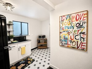 A kitchen with white cabinets, a black refrigerator, a double sink, and a microwave. There's a star-patterned floor and a wall with a colorful 'LOVE YOU' artwork. - The Creative Escape Community Canvas Loft (Coeur d'Alene)