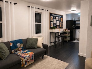 A living room with a sofa, a coffee table, and a dining area with chairs. There is a kitchen visible in the background. - The Creative Escape Community Canvas Loft (Coeur d'Alene)