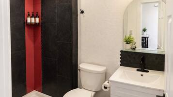 Um banheiro com vaso sanitário branco, box de chuveiro em vidro, parede com azulejos pretos e vermelhos, pia branca com torneira preta e um espelho acima da pia.