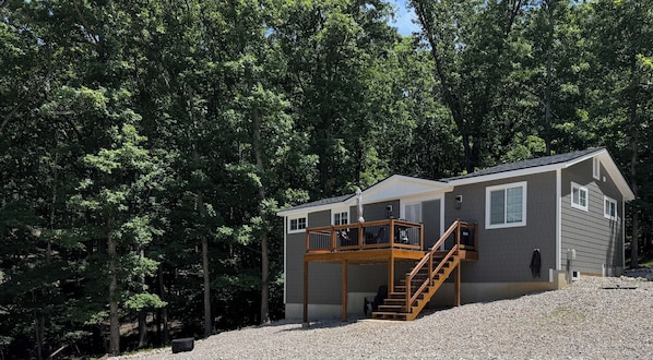 A two-story cabin with a wooden deck and stairs, surrounded by dense forest.
