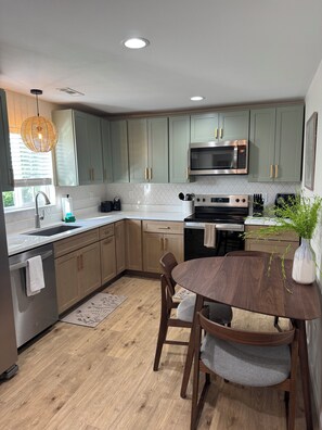 A modern kitchen with light green cabinets, a stainless steel microwave, a built-in oven, and a dining area with a wooden table and chairs.
