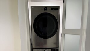 A laundry room with a stacked washer and dryer, a white door with frosted glass panels, and a light-colored wooden floor.