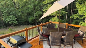 A wooden deck with a grill, wicker chairs, and a table.