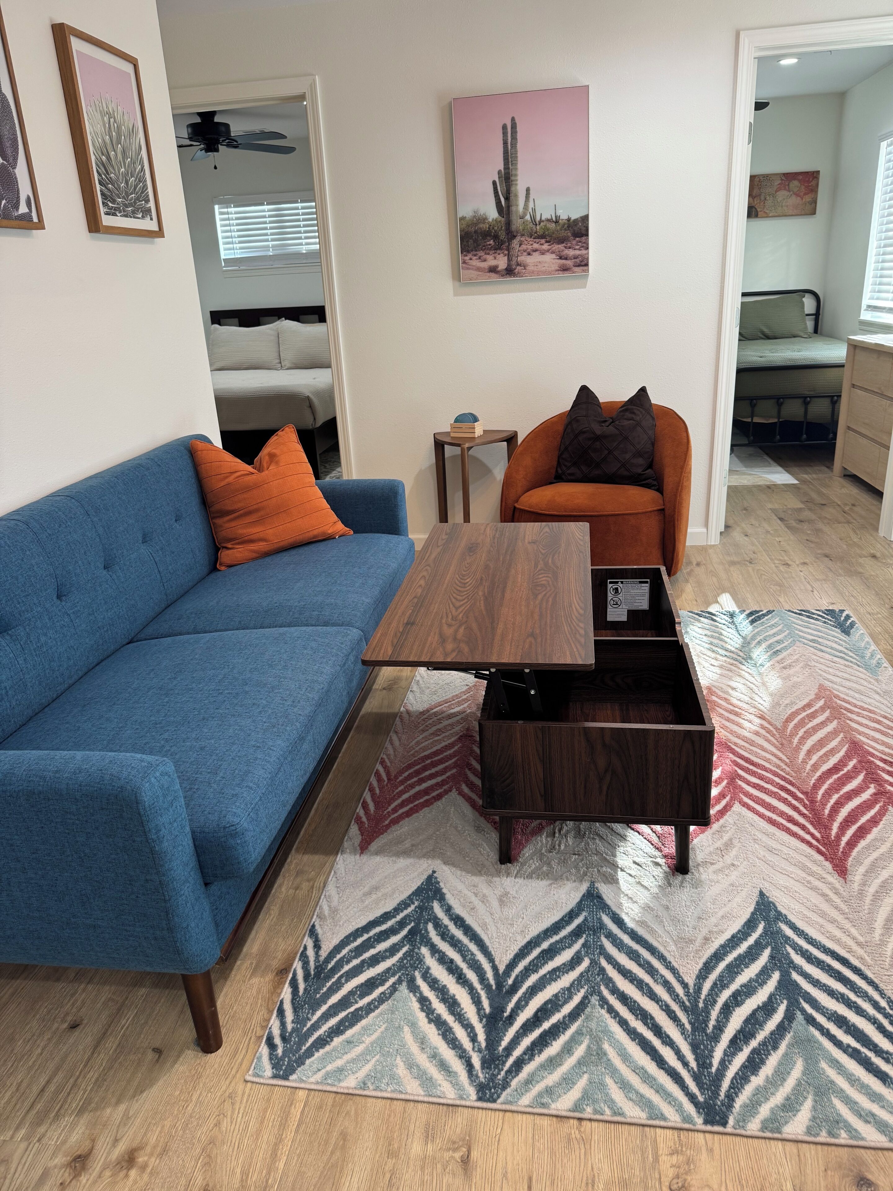 Una sala de estar con un sofá azul, un sillón naranja, una mesa de centro de madera y una alfombra estampada.