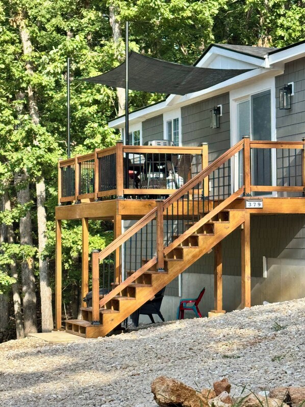 A wooden deck with a staircase leading to a covered area, surrounded by trees.