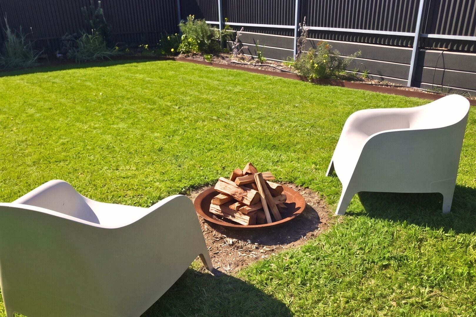 A backyard with a fire pit and two white chairs.