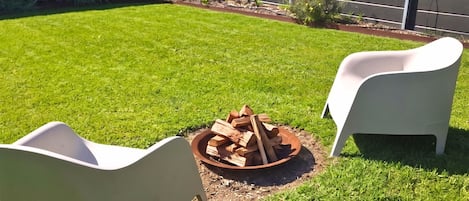 A backyard with a fire pit and two white chairs.