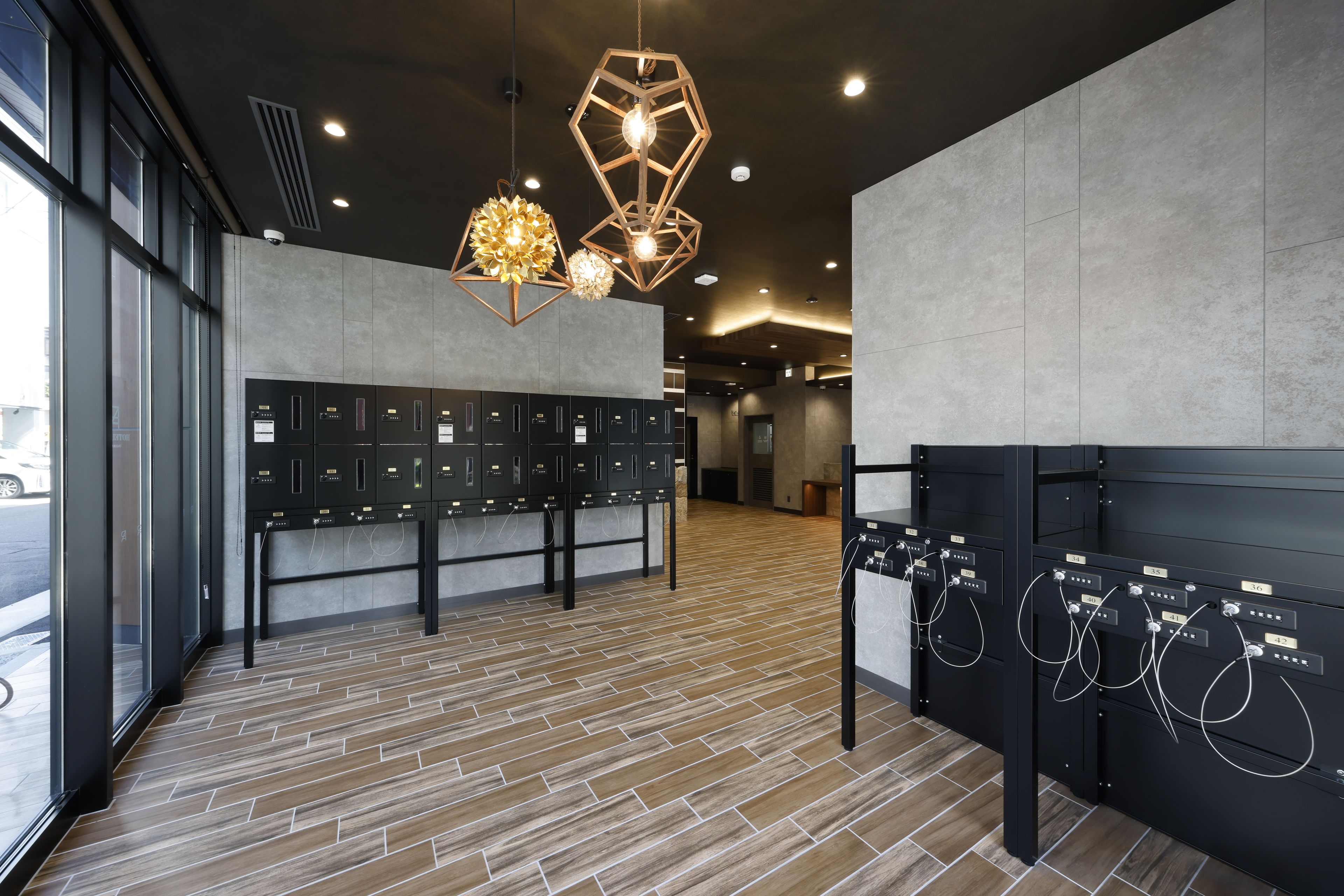 A modern hotel lobby with a wood-patterned floor, a row of black lockers, and geometric pendant lighting.