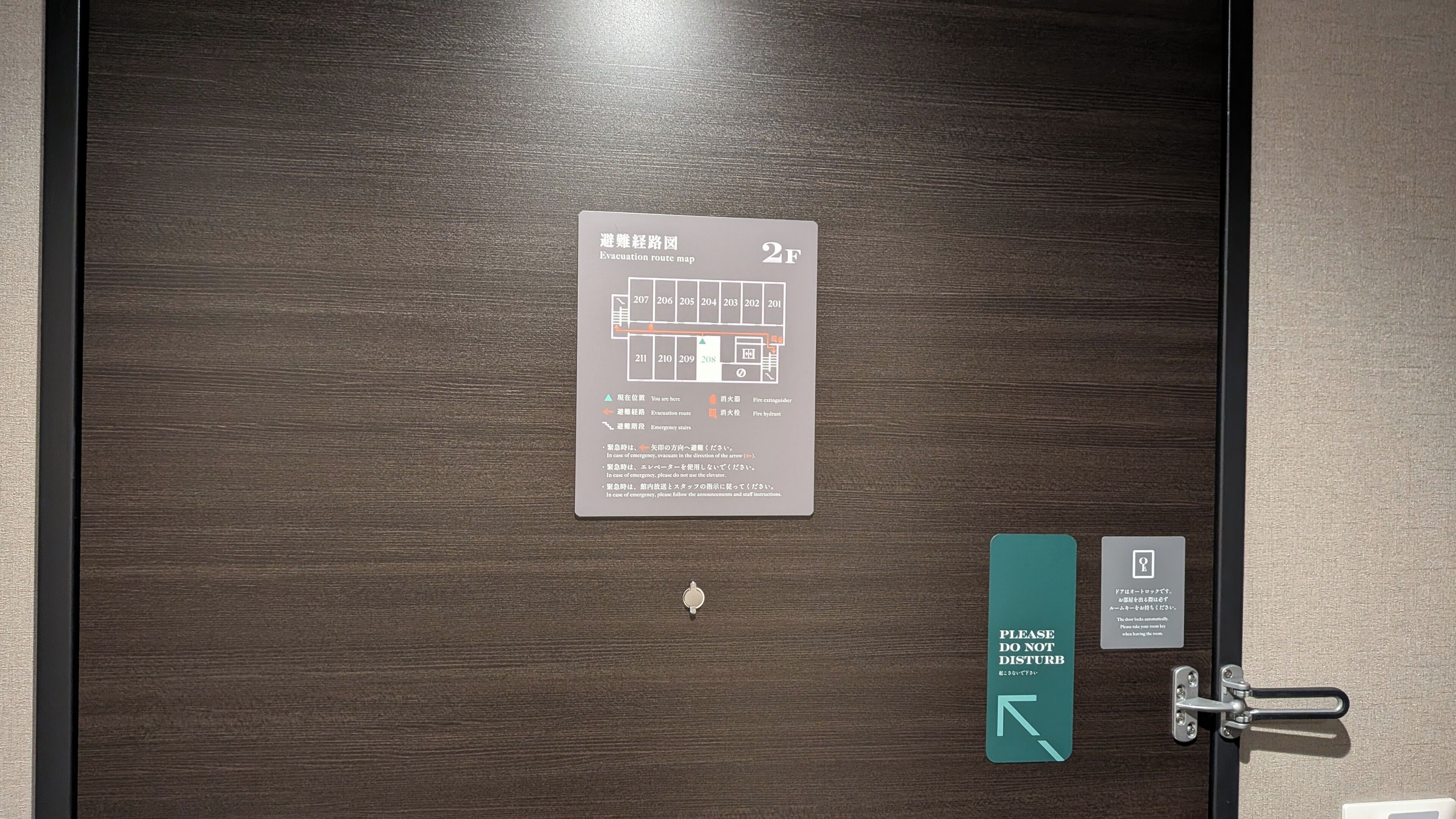 A hotel room door with an evacuation route map and a 'Please Do Not Disturb' sign.