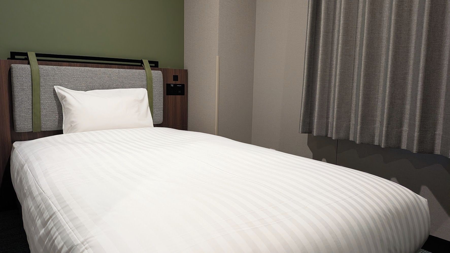 Habitació d'hotel amb un llit, capçalera i cortines.