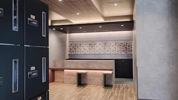 A modern hotel lobby with a central seating area, a patterned wall, and a series of lockers on the left.