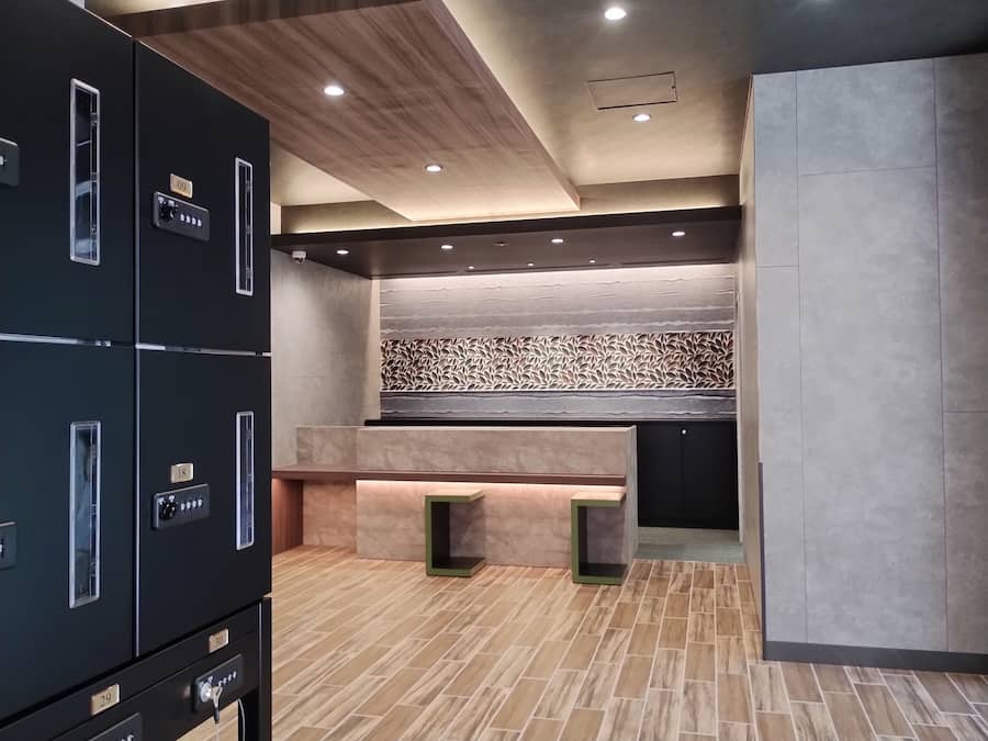 A modern hotel lobby with a central seating area, a patterned wall, and a series of lockers on the left.