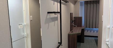 A hotel room with a bed, a desk, a chair, a wardrobe, and a window with curtains.