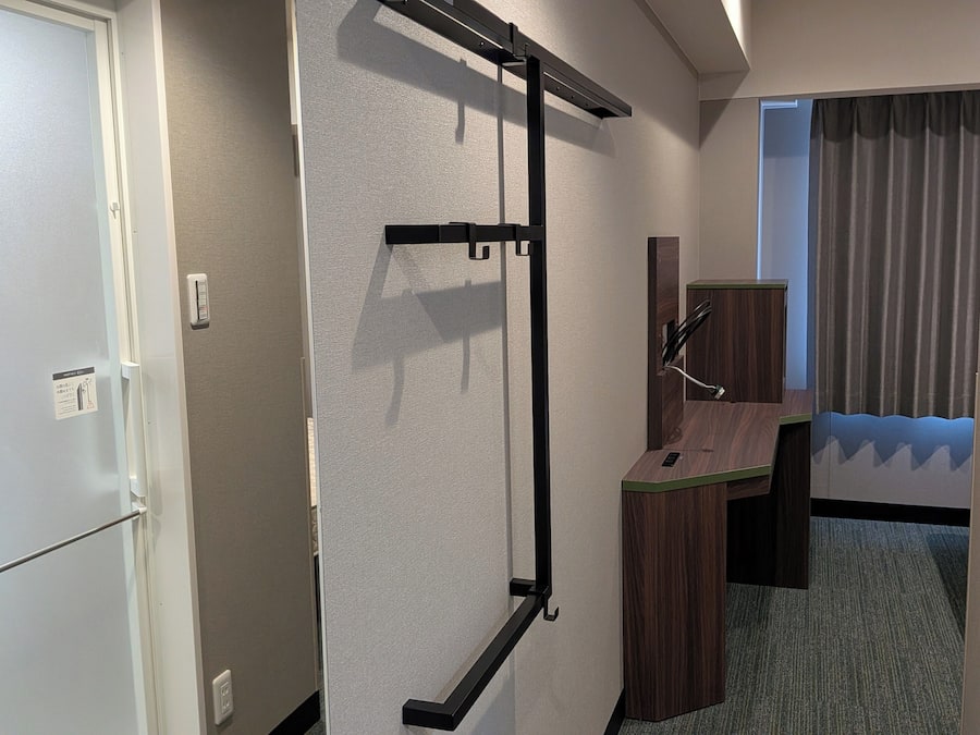 A hotel room with a bed, a desk, a chair, a wardrobe, and a window with curtains.