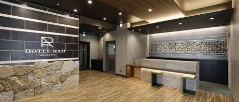 A hotel reception area with a stone wall, a reception desk, and a modern ceiling design.