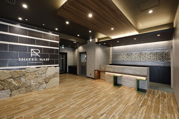 A hotel reception area with a stone wall, a reception desk, and a modern ceiling design.
