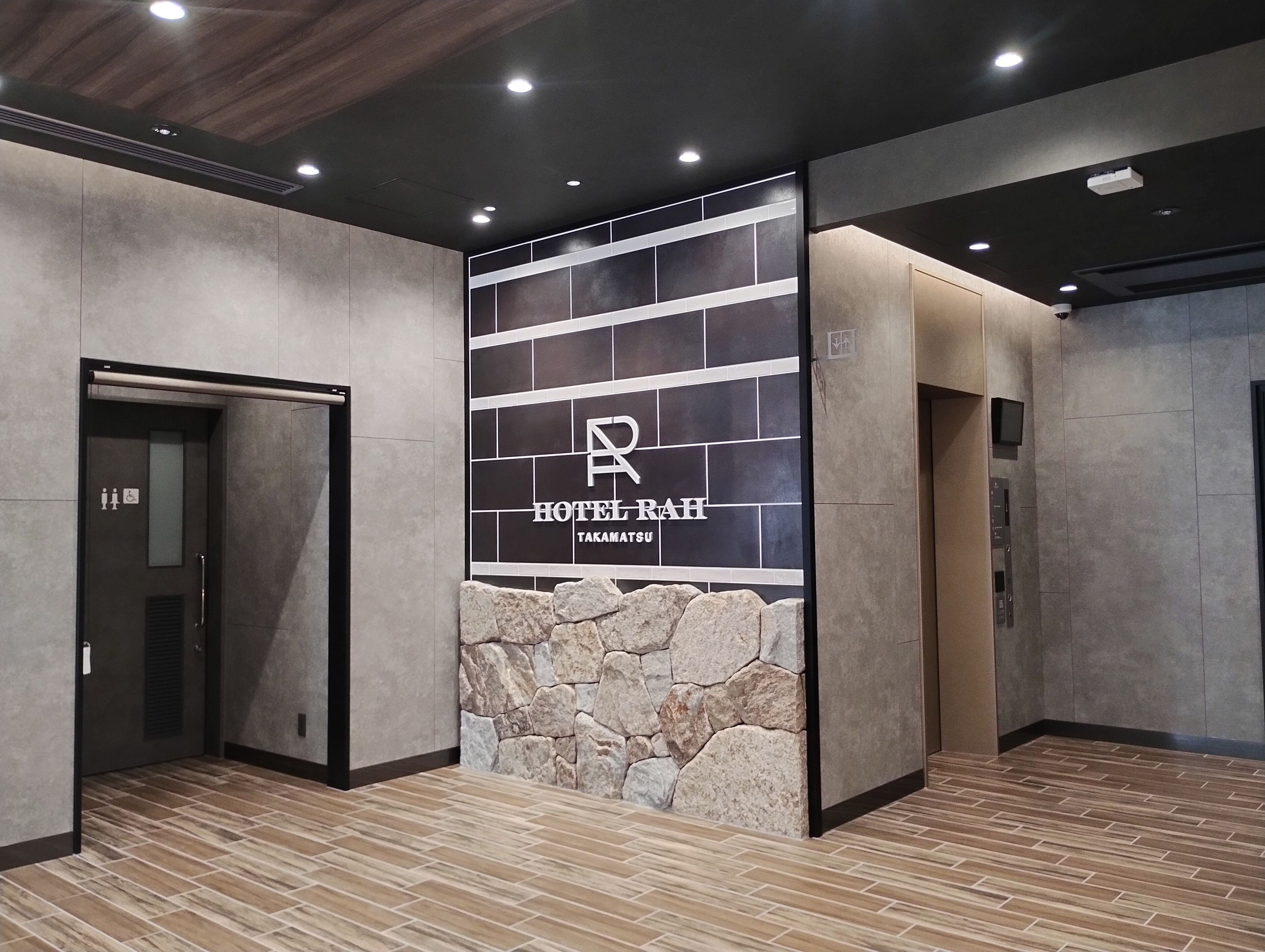 Un hall d’hôtel moderne avec un mur d’accent en pierre, un comptoir d’accueil et un ascenseur.