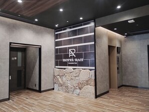 A modern hotel lobby with a stone accent wall, a reception desk, and an elevator.