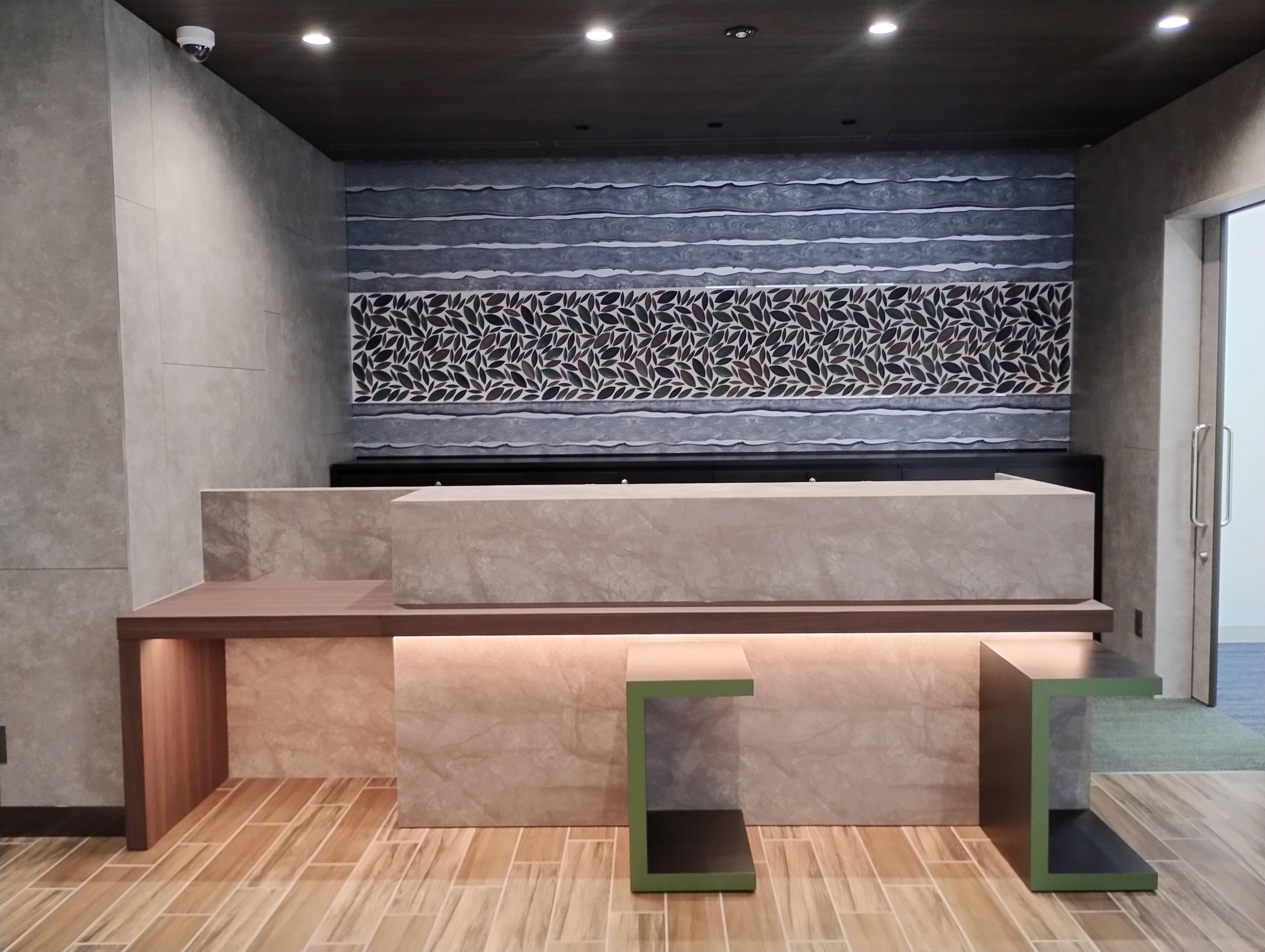 Un mostrador de recepción de diseño moderno, una pared con un estampado llamativo detrás y una cámara de seguridad en el techo.