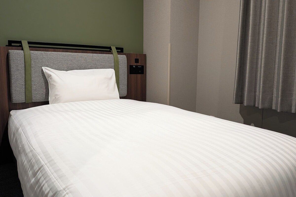 Una habitación de hotel con cama, cabecera y cortinas.