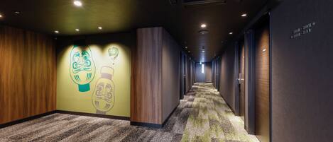 A hotel corridor with a carpeted floor, wooden panel walls, and a ceiling with recessed lighting.